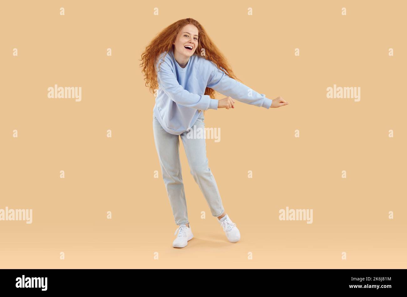 Porträt von lustigen fröhlichen jungen Frau in lässigem Outfit tanzen auf beigefarbenem Studiohintergrund Stockfoto