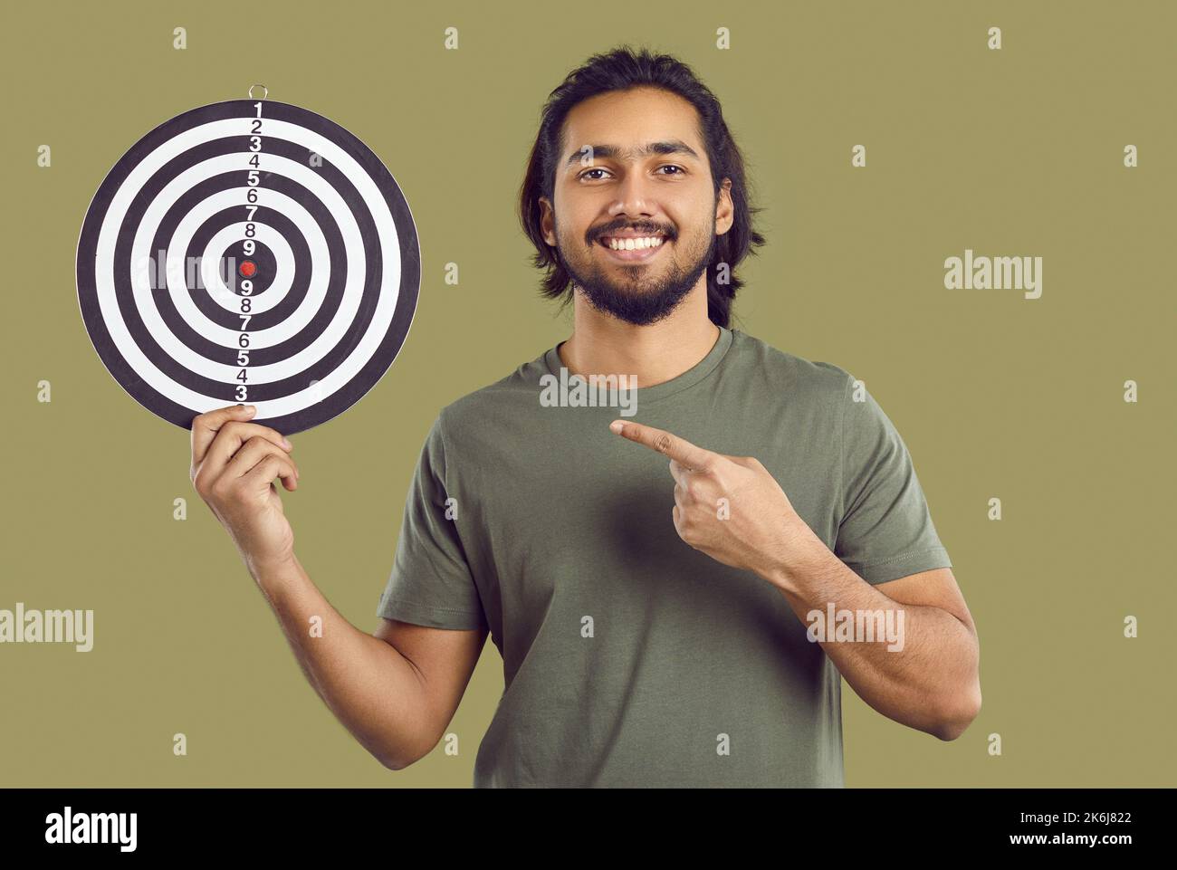 Glücklicher Inder, der sich das Ziel gesetzt hat, mit dem schießigen Ziel und dem Zeigefinger auf das Bullseye zeigt Stockfoto