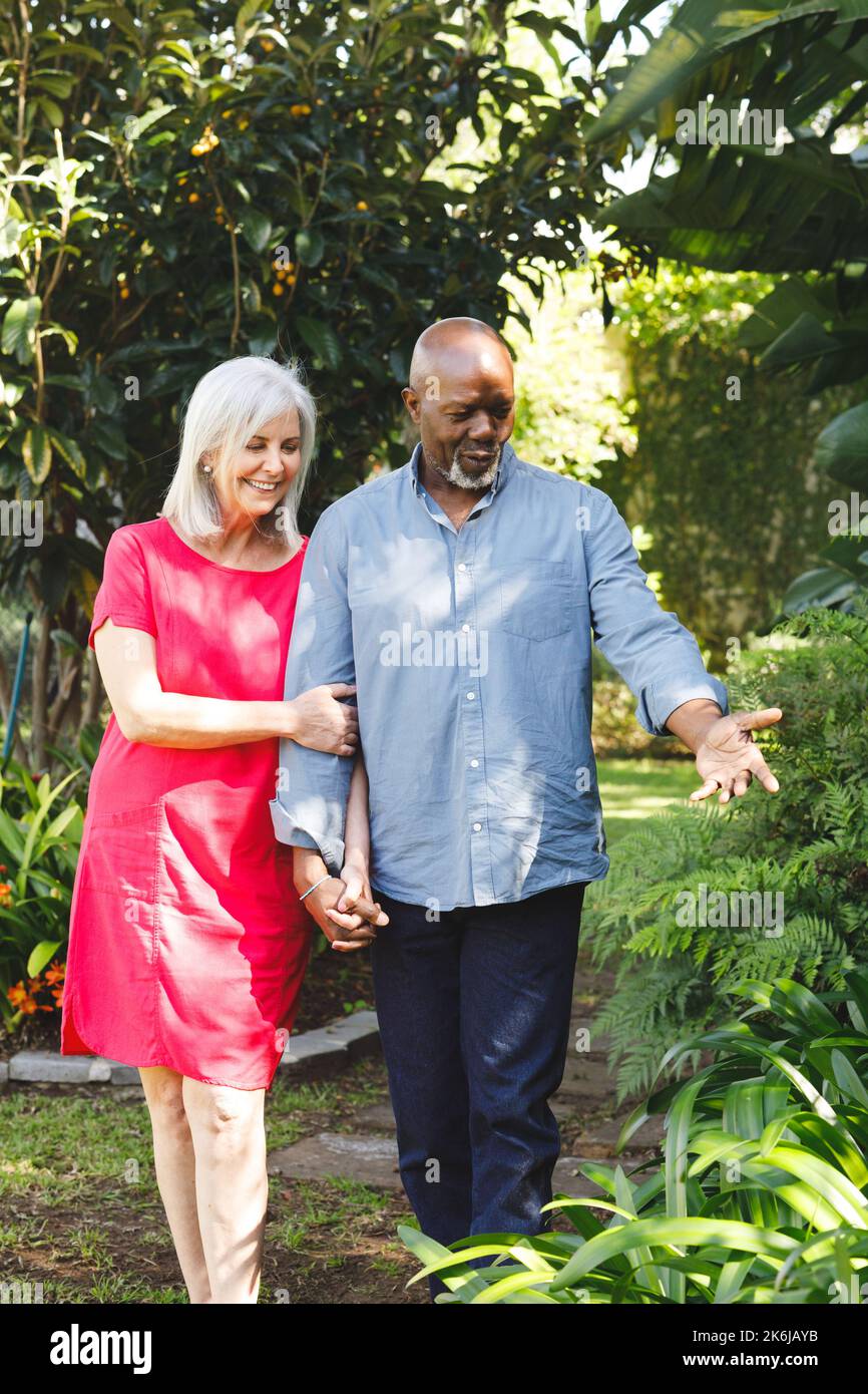 Glückliches älteres, vielfältiges Paar, das im Garten spaziert Stockfoto