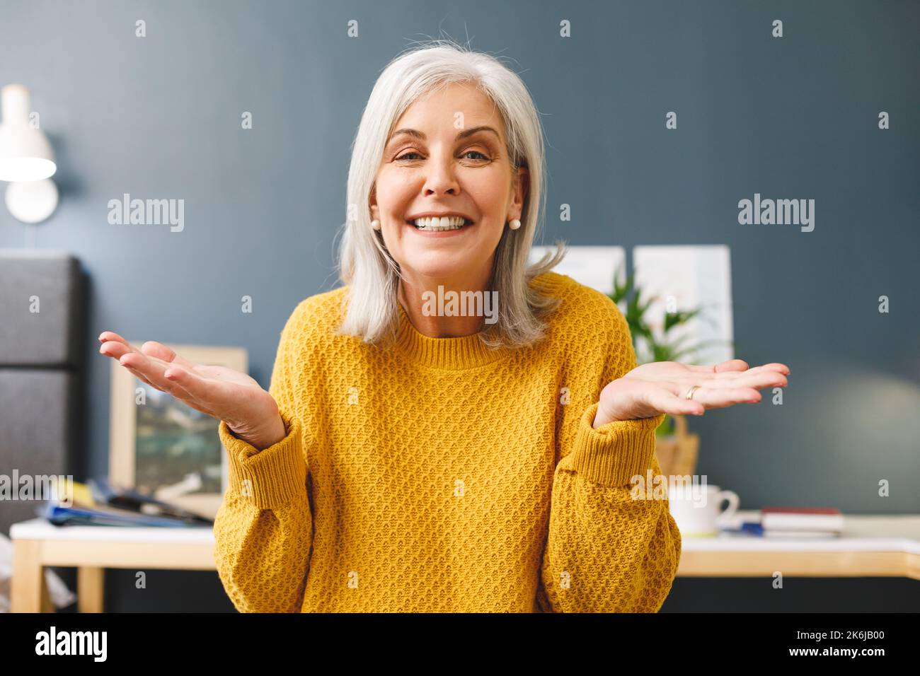 Glückliche weisse Seniorin, die zu Hause Videoanrufe tätigt, lächelt und Gesten mit den Händen vor die Kamera macht Stockfoto