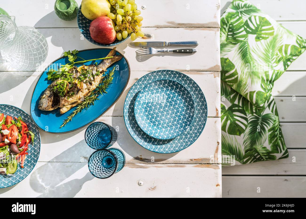 Im Ofen gebackene Goldbrasse, auch bekannt als Orata, wird auf einem weißen Holztisch mit Gemüsesalat und Obst serviert. Gesunde Zubereitung von Meeresfrüchten Stockfoto