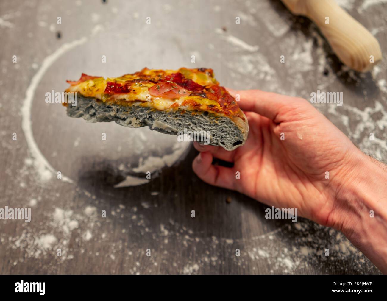 Nahaufnahme einer Person, die ein Stück Pizza aus grauem, hausgemachtem Teig hält. Innovative italienische Küche. Stockfoto