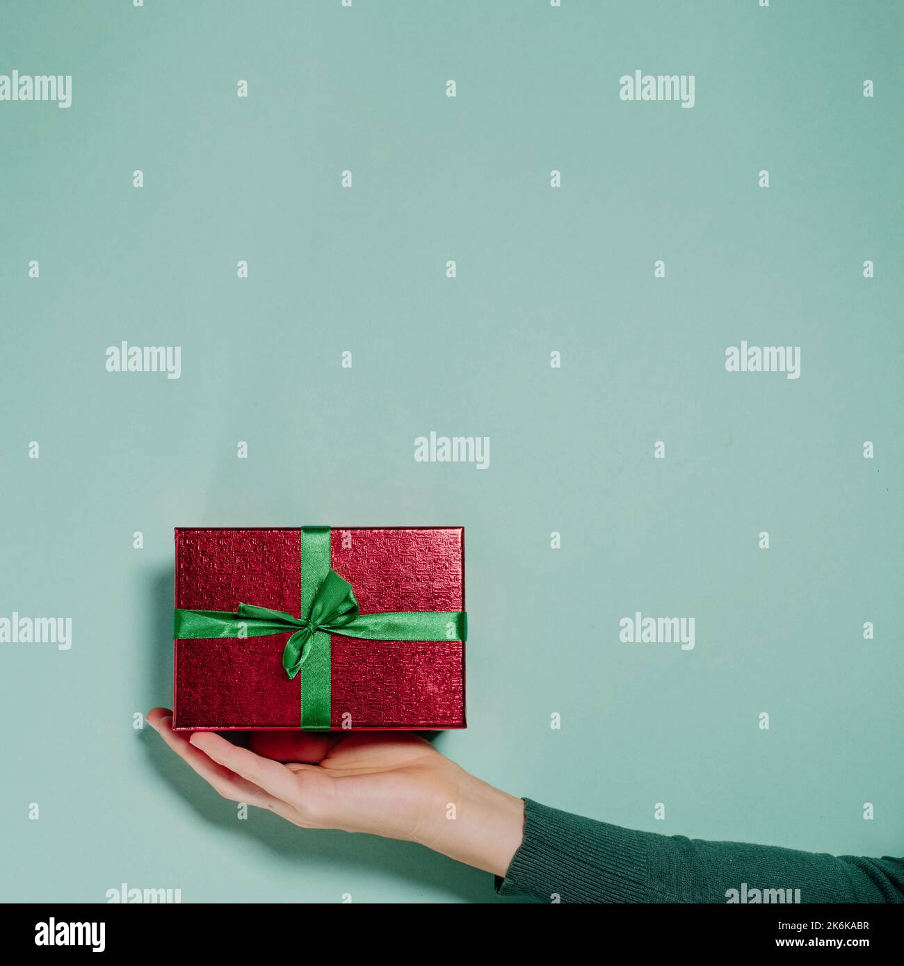 Präsent auf der Hand über dem schlichten Hintergrund. Minimalistisches Christmass- oder Valentine-Gist-Konzept mit Kopierraum. Rotes Paket mit Schleife zum Geburtstag oder Stockfoto