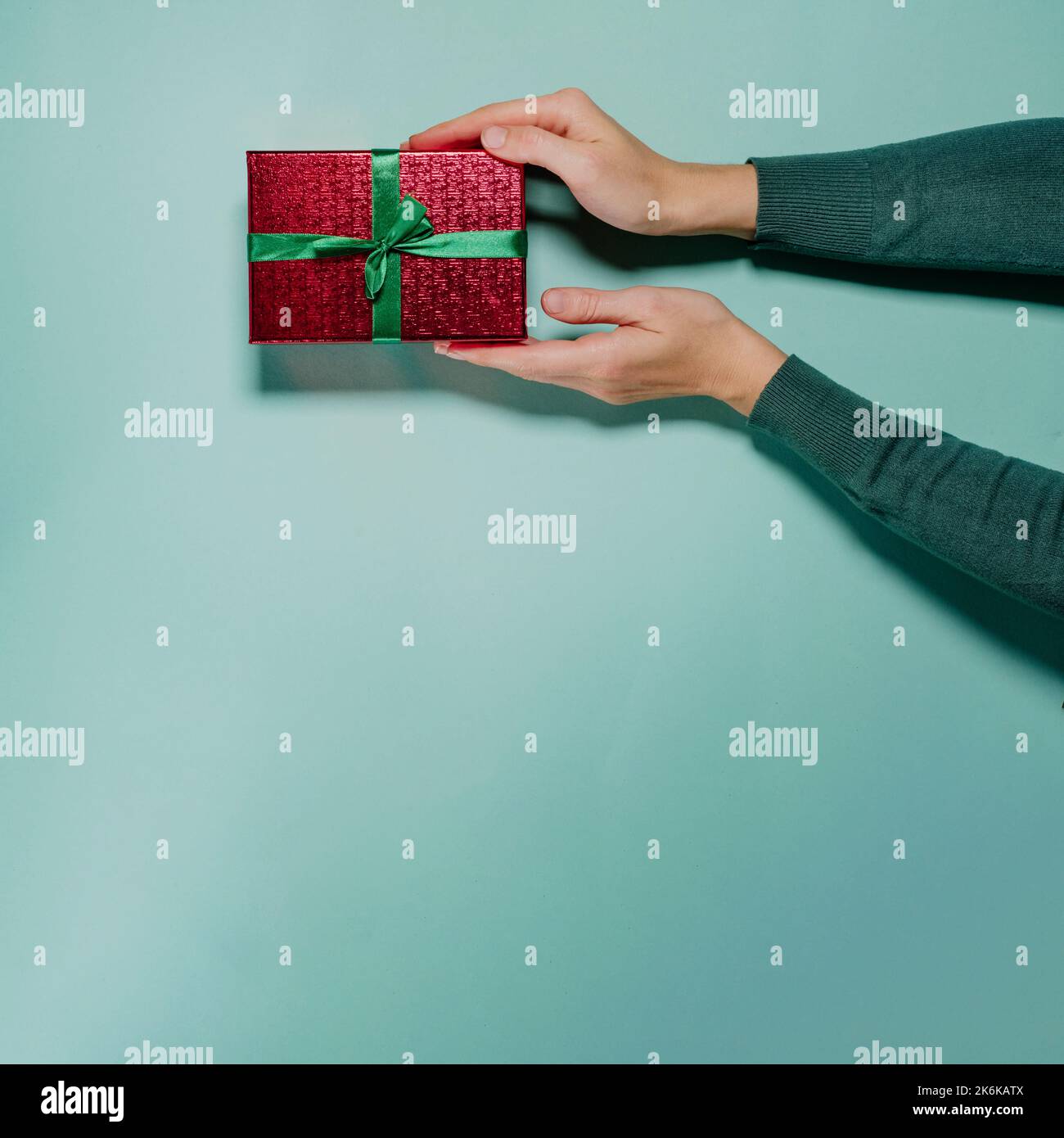 Präsent auf der Hand über dem schlichten Hintergrund. Minimalistisches Christmass- oder Valentine-Gist-Konzept mit Kopierraum. Rotes Paket mit Schleife zum Geburtstag oder Stockfoto