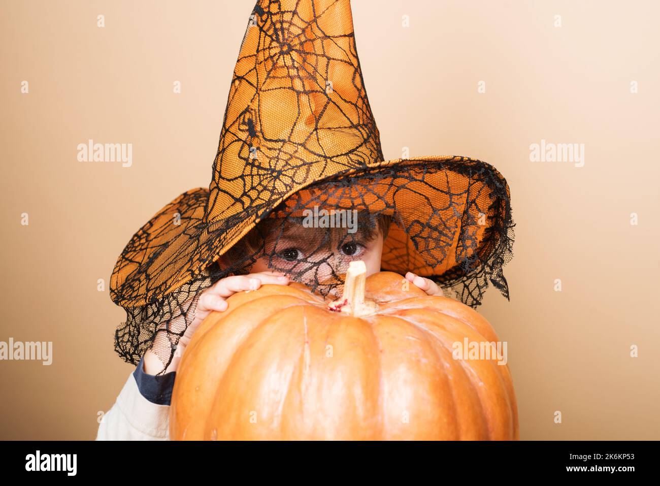 Kind im Hexenhut versteckt sich am halloween Kürbis. Karnevalskostüm. Jack-o-Laterne. Trick or Treat. Stockfoto