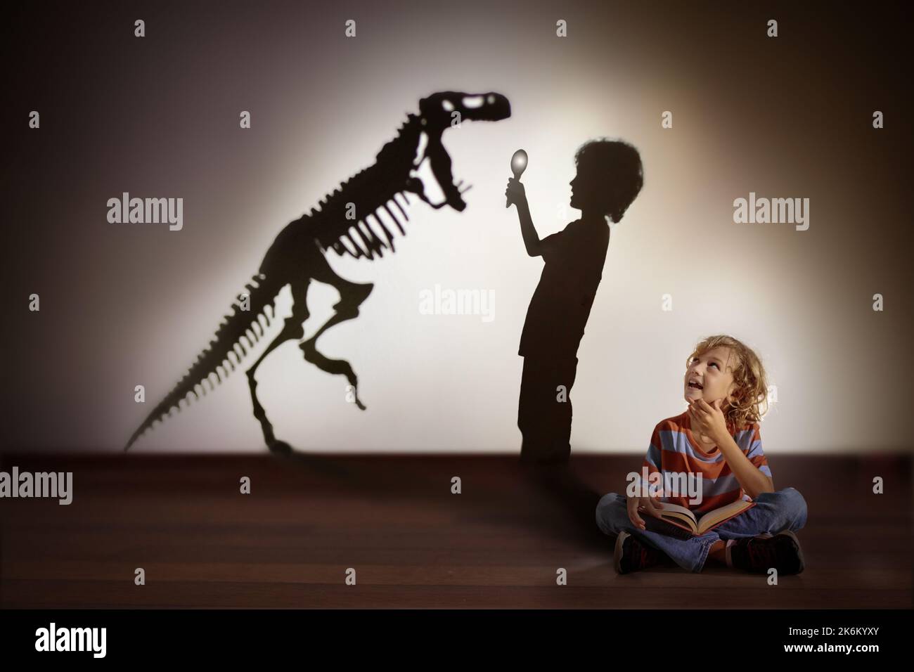 Dinosaurier Schatten im Kindertraum. Kinder lesen Buch und stellen sich die Zukunft vor. Kleiner Junge, der träumt, Paläontologe zu werden. Kinder lesen. Stockfoto