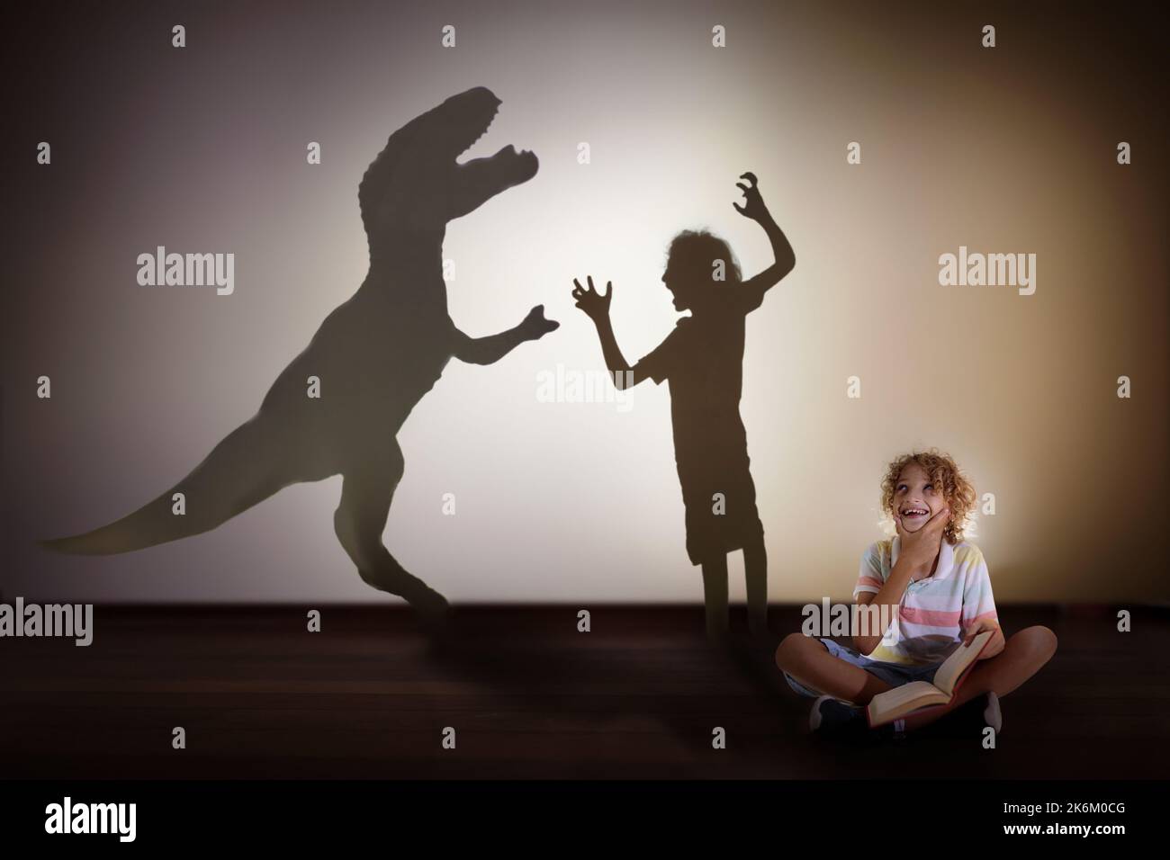 Dinosaurier Schatten im Kindertraum. Kinder lesen Buch und stellen sich die Zukunft vor. Kleiner Junge, der träumt, Paläontologe zu werden. Kinder lesen. Stockfoto