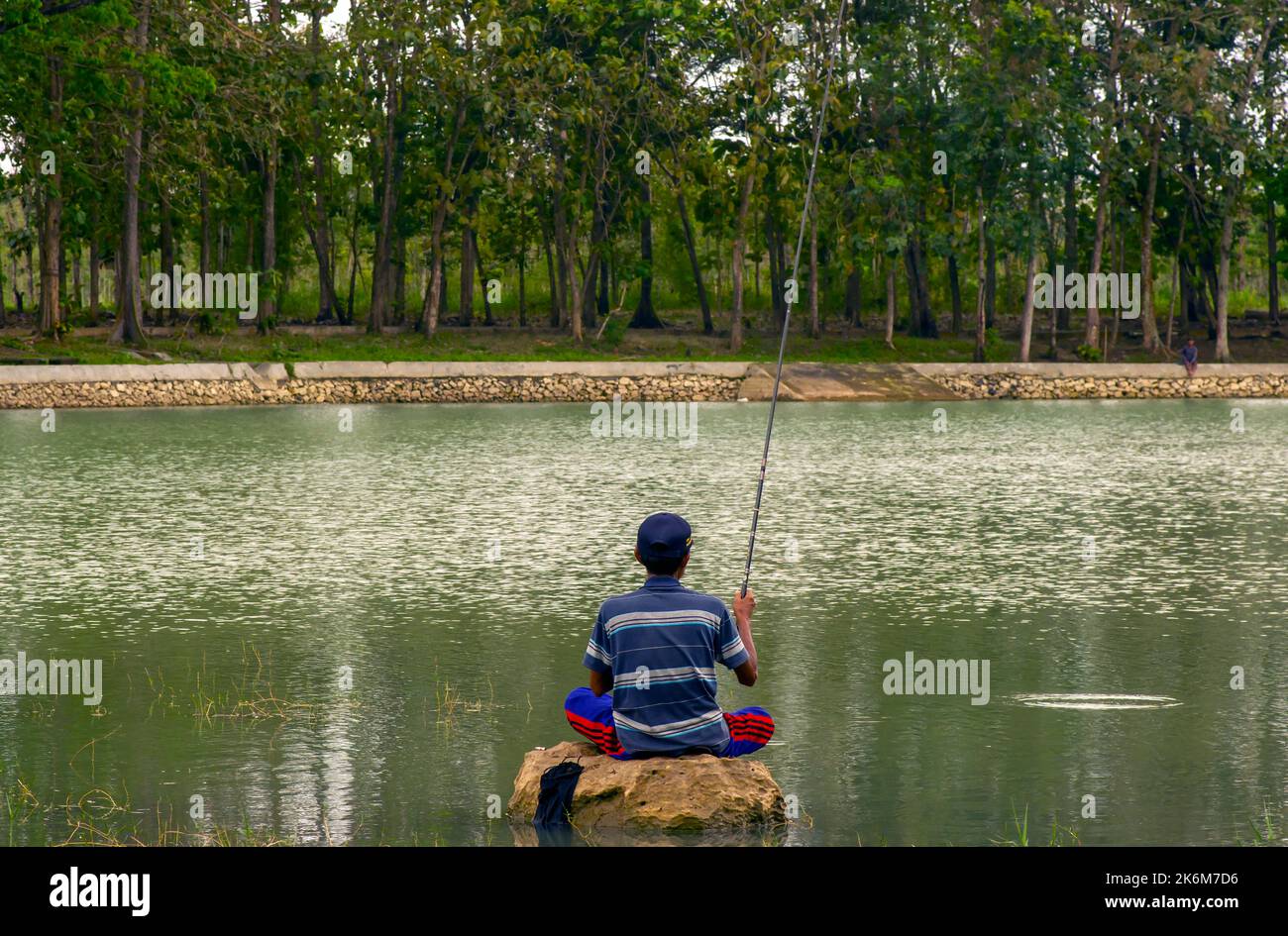 Yogyakarta, Indonesien - 11. August 2022: Mann entspannt sich und angeln sitzt auf dem Stein, in Gunung Kidul, Yogyakarta, Indonesien Stockfoto