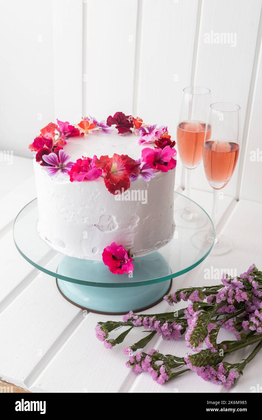 Schöne Dekoration der Hochzeitstorte mit weißer Creme und essbaren Blumen, neben zwei Gläsern mit Champagner, Essen als Dessert in der Feier, Tisch Stockfoto