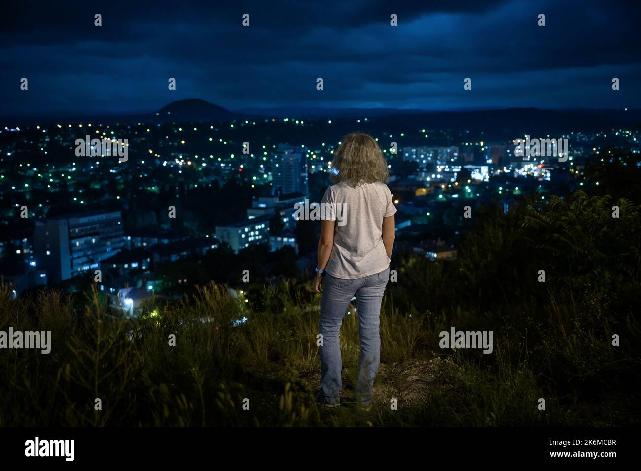 Panorama von Pyatigorsk bei Nacht, Russland. Junge Frau steht auf Stadt und Himmel Hintergrund, Person Tourist schaut auf Stadt Lichter von Berggipfel in summe Stockfoto