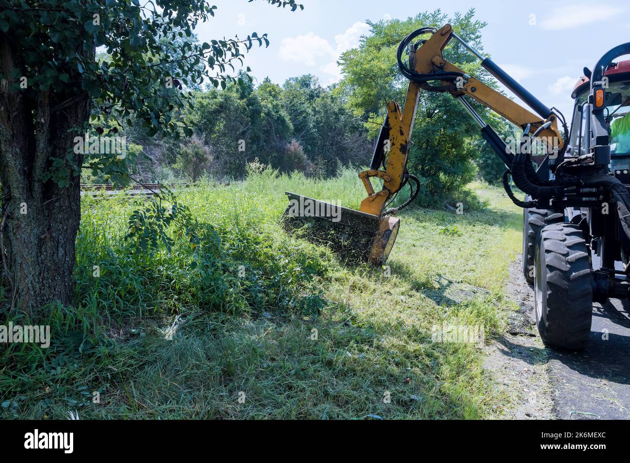 Stadtarbeiter, die mit einem mechanischen Mäher fahren, der Gras auf der Straße mäht, während der Straßenmeisterdienste auf der Autobahn am Straßenrand durchgeführt wird Stockfoto