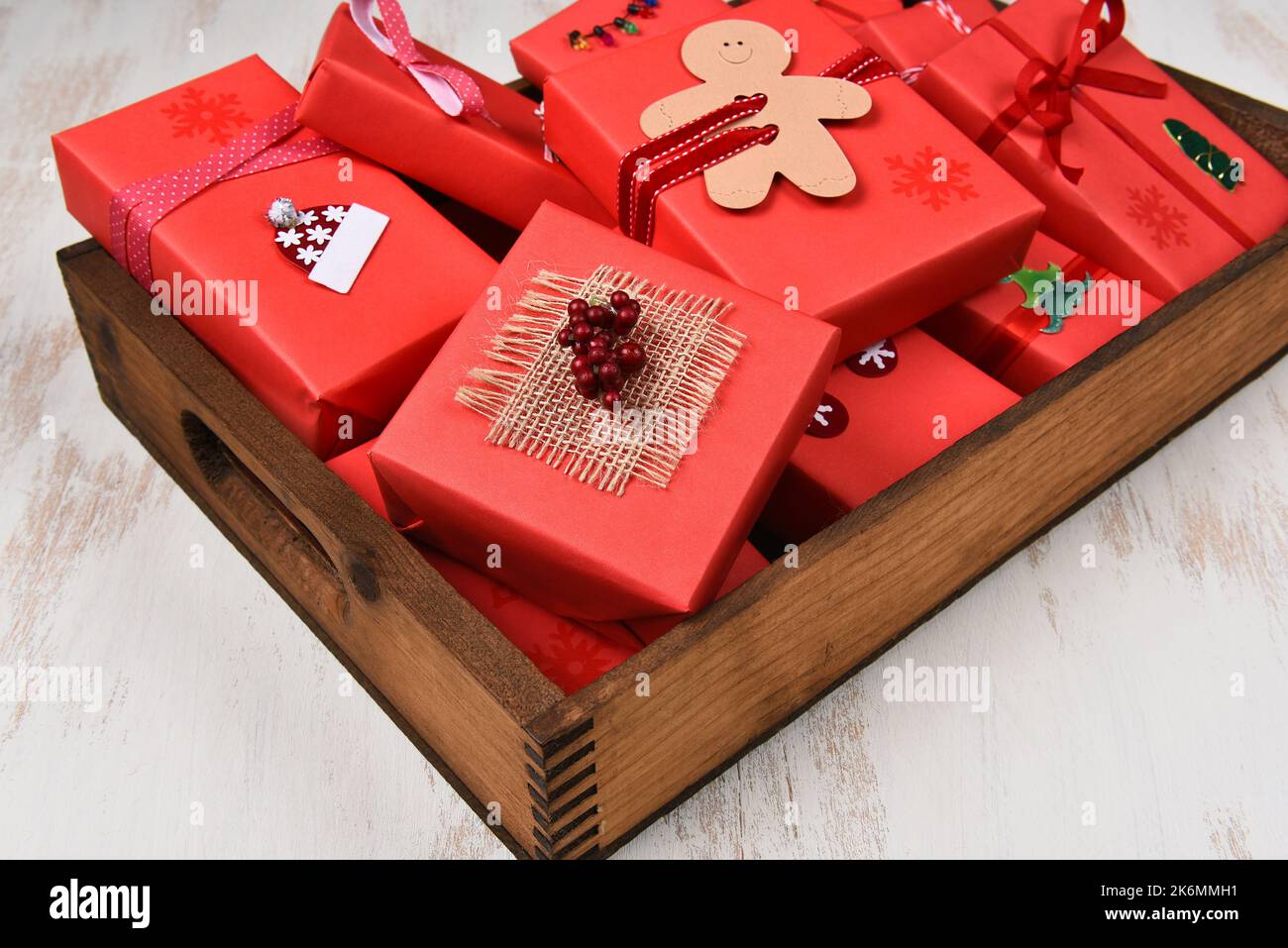 Weihnachtsgeschenke. Nahaufnahme von Geschenken, eingewickelt und in rotem Papier in einer dunklen Holzkiste dekoriert. Stockfoto