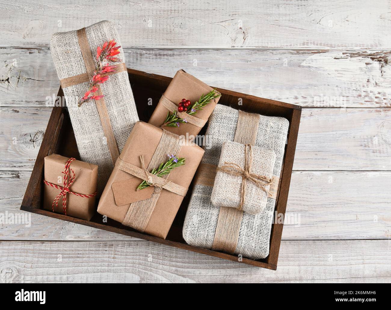Weihnachtsgeschenke. In einer Holzkiste verpackte Geschenke aus Sackleinen und braunem Papier. Stockfoto