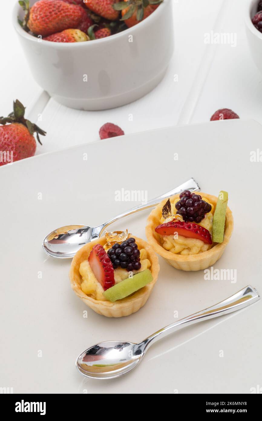 Details von Dessert mit Erdbeeren, Brombeeren und Gebäck-Creme, Tapete von eleganten Tellern mit silbernen Löffeln, Gebäck dekoriert Stockfoto