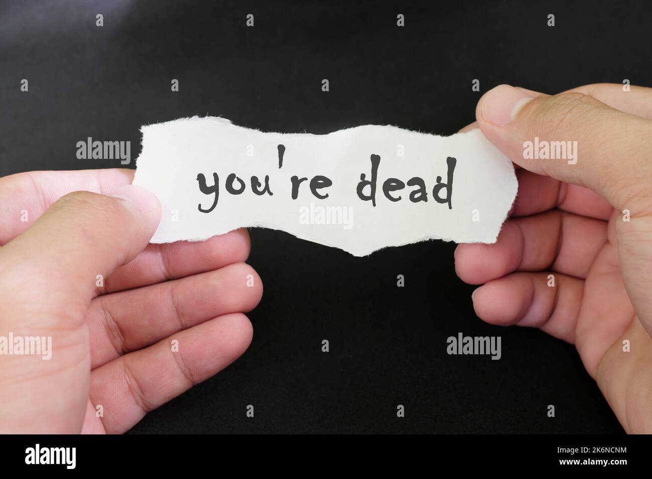 Konzept der Todesbedrohung. Menschliche Hände halten eine Papiernotiz mit geschriebenem Wort Sie sind tot in dunkelschwarzem Hintergrund. Stockfoto
