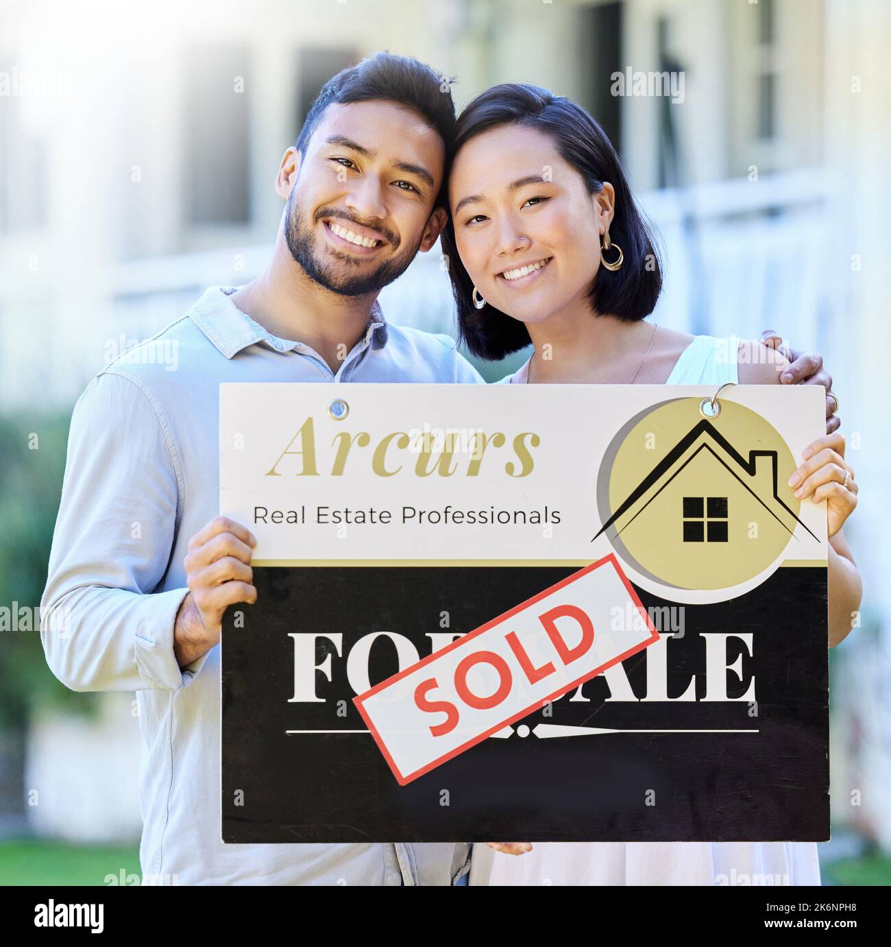 Es wird offiziell verkauft. Ein junges Paar hält ein verkauftes Brett vor ihrem Haus. Stockfoto