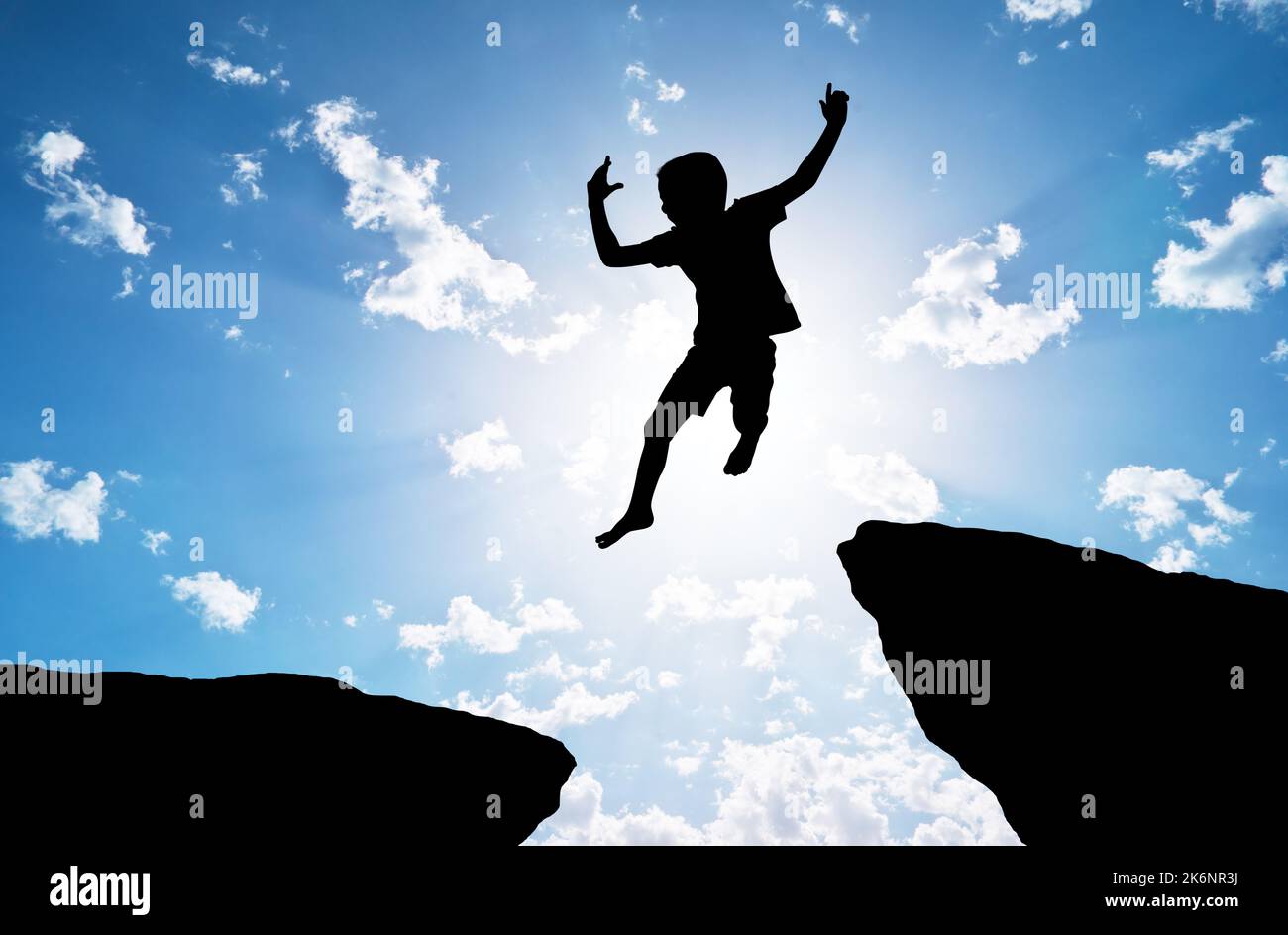 Glückliche Silhouette des Jungen springt über eine Klippe. Emotionale und kokeptuelle Szene. Stockfoto