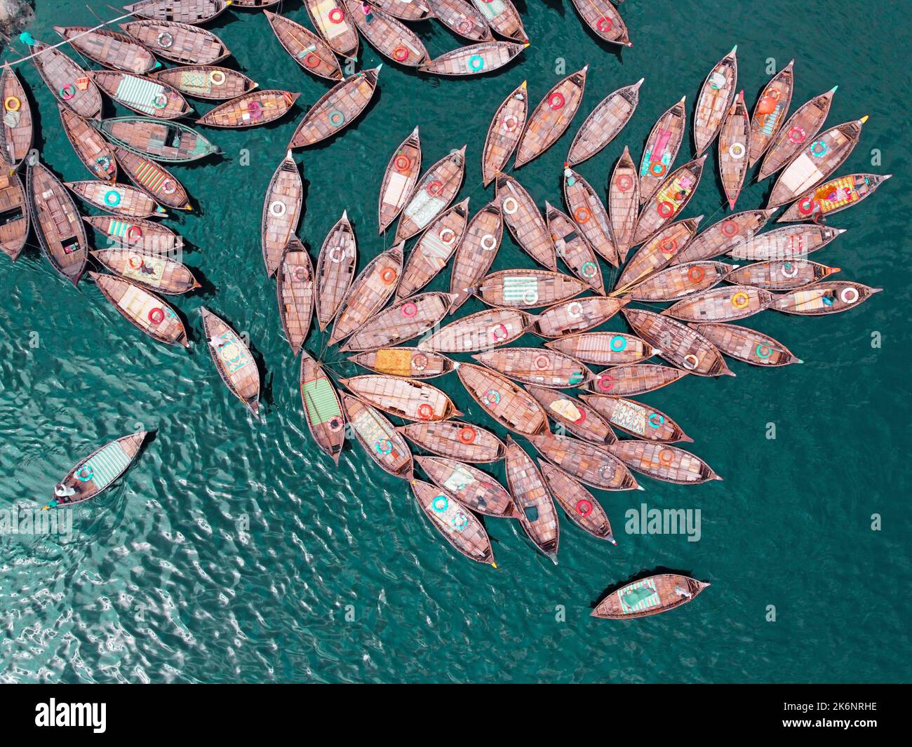 Hunderte von Holzbooten ziehen sich in Mustern um ihre Anlegestellen herum, die wie Blütenblätter aussehen, um am Morgen auf dem Fluss Buriganga zu pendeln. Stockfoto