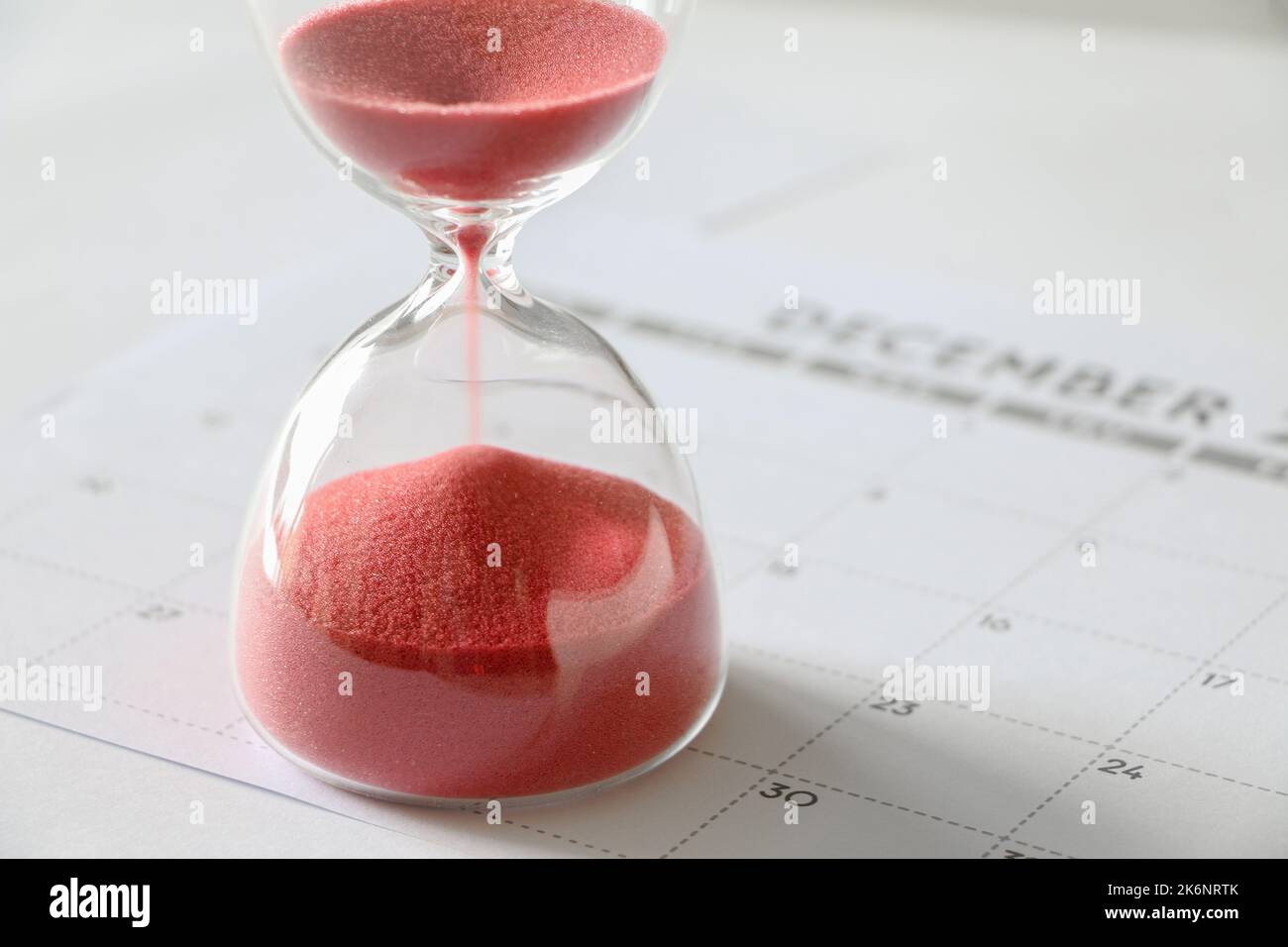 Roter Sand, der durch Sanduhr-Birnen läuft, im Dezember-Kalender, den Zeitverlauf, das Jahresende, das Konzept der Zeitüberschreitung misst Stockfoto