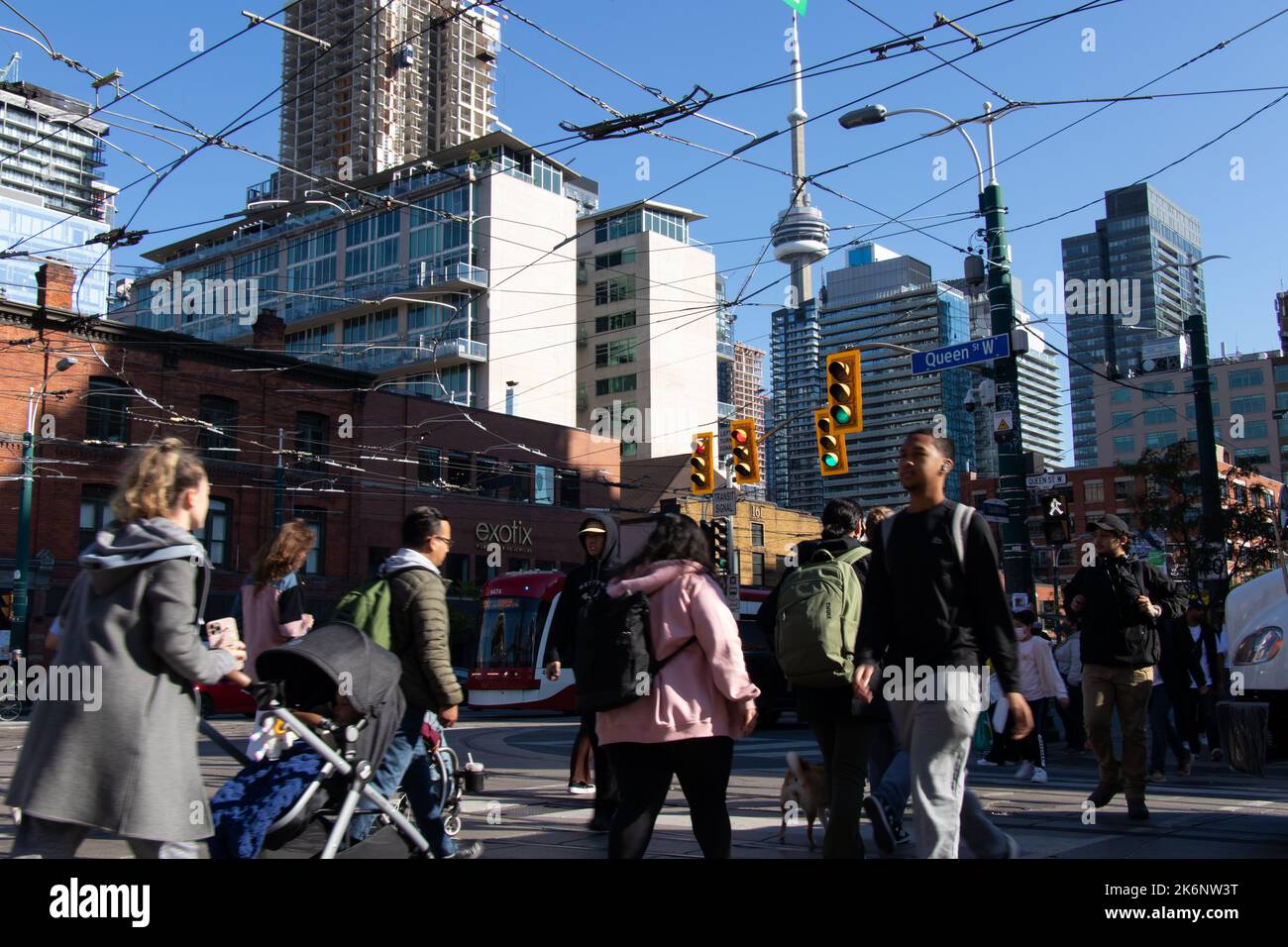 Die Leute gehen über die Queen St. in der Spadina Ave. In der Hauptverkehrszeit am Nachmittag kann man den CN Tower im fernen Hintergrund sehen. Stockfoto