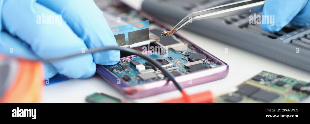 Hände in Handschuhen halten einen Smartphone-Mikrochip mit einer Pinzette Stockfoto