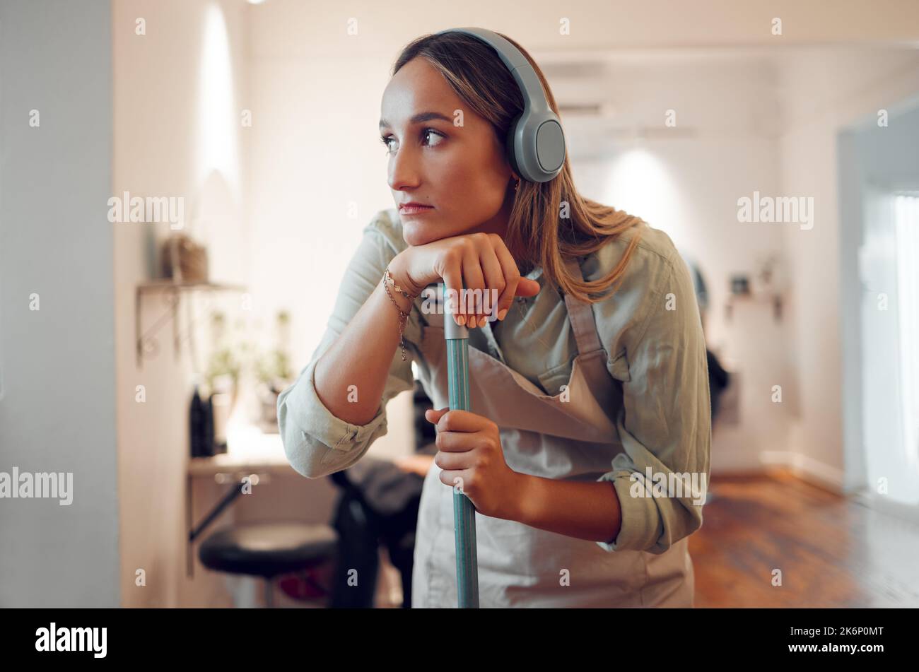 Frau, müde und putzte mit Kopfhörern für Musik, während sie im Zimmer zu Hause arbeitete. Sauberer, denkender und nachdenkender beim Hören von Radio, Podcast Stockfoto