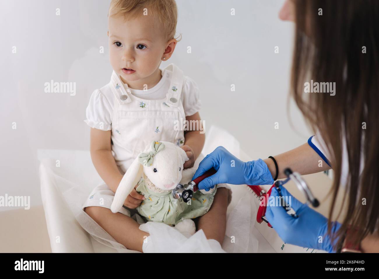 Freundliche Ärztin überprüft mit Stethoskop weiches Spielzeug Kaninchen. Anpassung des kleinen Babys an den jungen Arzt Kinderarzt. Es ist nur ein Spiel Stockfoto