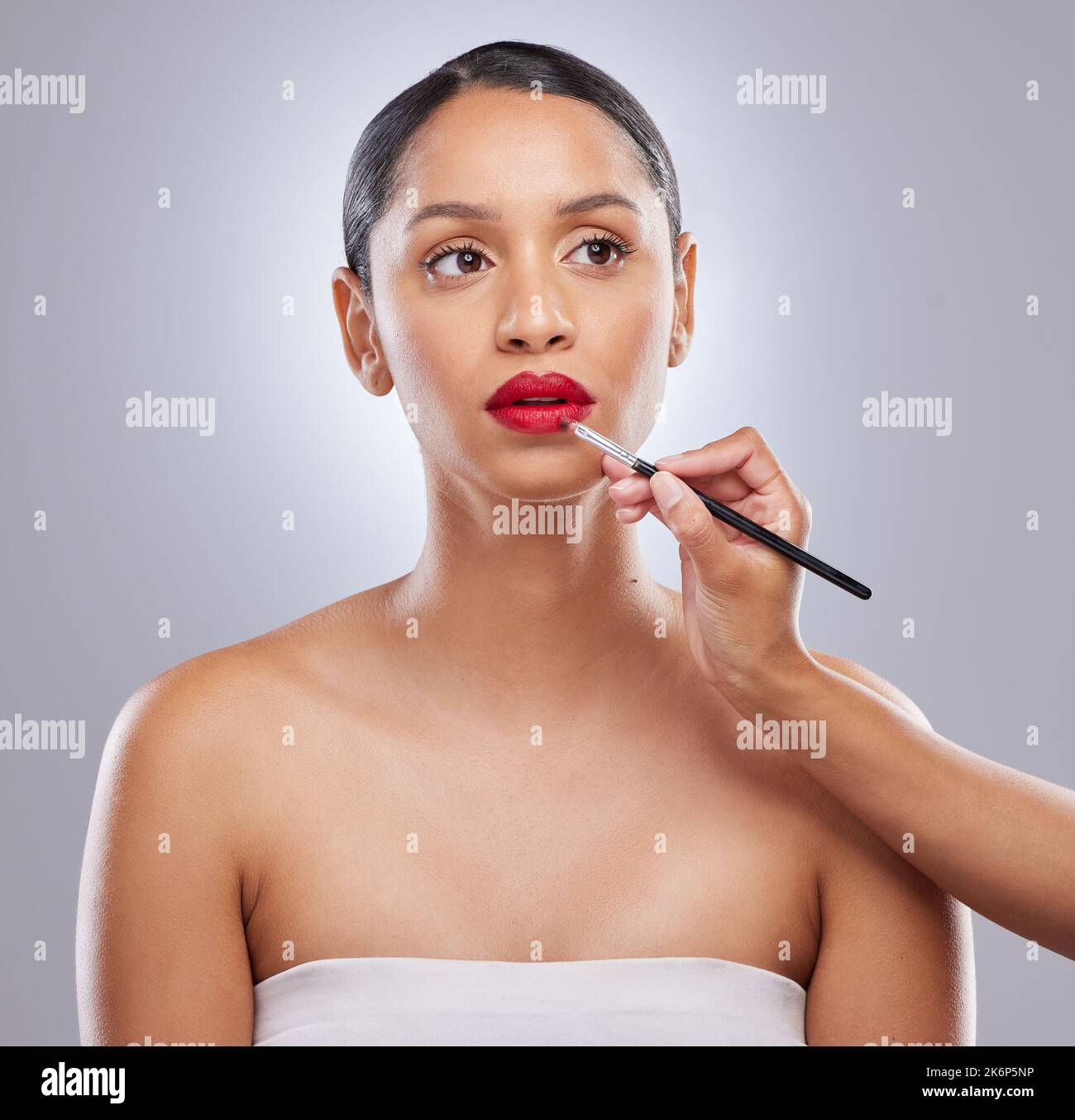 Die Stadt rot malen. Eine attraktive junge Frau, die im Studio steht, während ein Make-up-Künstler Lippenstift aufträgt. Stockfoto