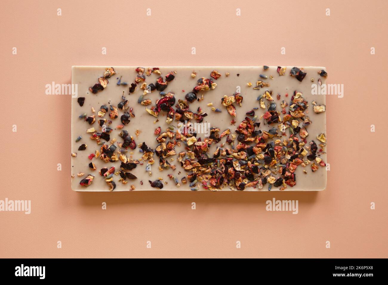 Rosafarbene Schokolade mit Nüssen und Beeren. Süßes leckeres handgemachtes Schokoladenstäbchen auf rosafarbenem Hintergrund Stockfoto