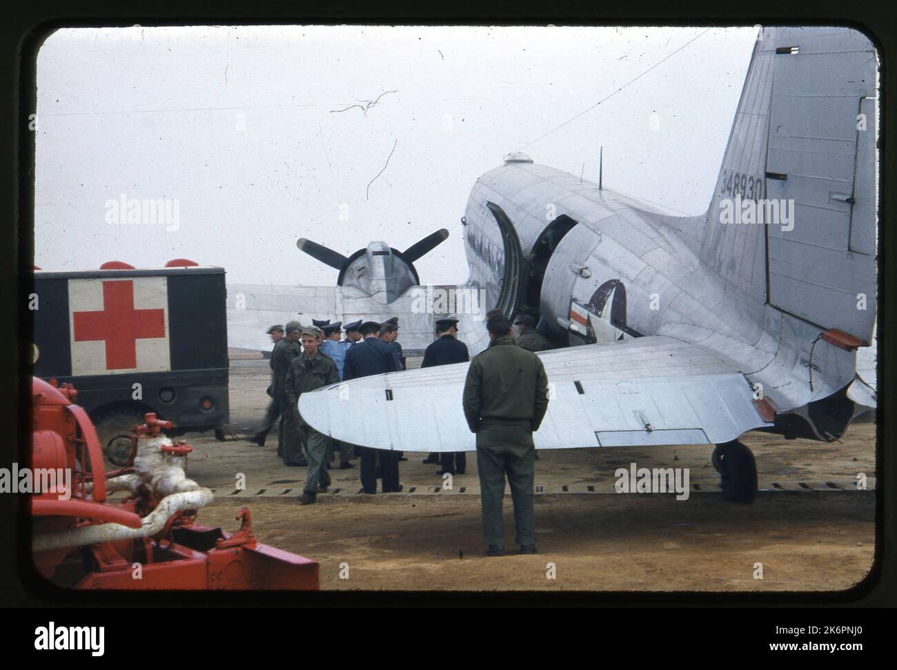 Dreiviertel linke Seitenansicht eines Douglas C-47B Skytrain (s/n 43-48930; c/n 14747-26191)-Flug mit dem Flugzeug, irgendwo in Korea. Ein Krankenwagen wird links vom Flugzeug geparkt, und eine Gruppe von Männern steht neben dem Flugzeug in der Nähe der Flugzeugtür, die geöffnet ist. In der unteren linken Ecke des Bildes wird die Stützausrüstung angezeigt. Stockfoto