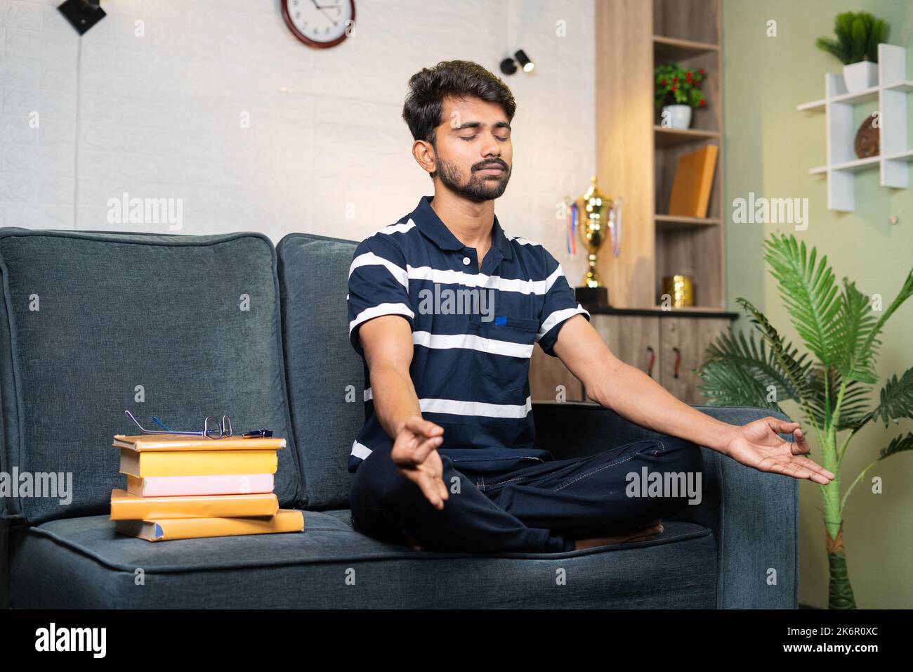 Junge indische Studentin meditiert vor der Vorbereitung zum Studium zu Hause - Konzept der Meditation, gesunder Lebensstil und Stressabbau. Stockfoto