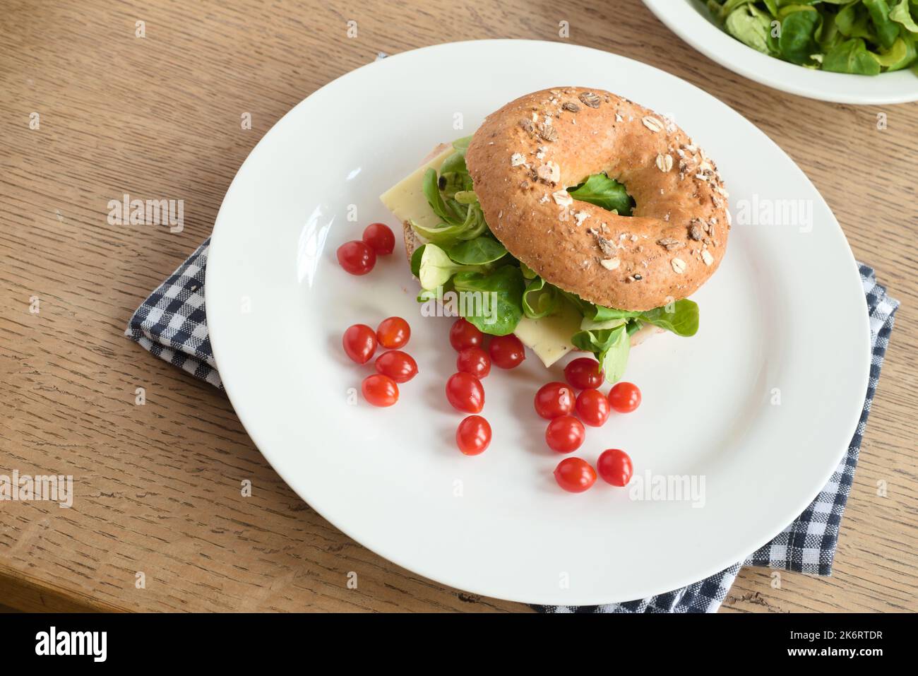 Bagel-Sandwich mit Käse, grünen Salatblättern und Kirschtomaten auf einem Teller Stockfoto