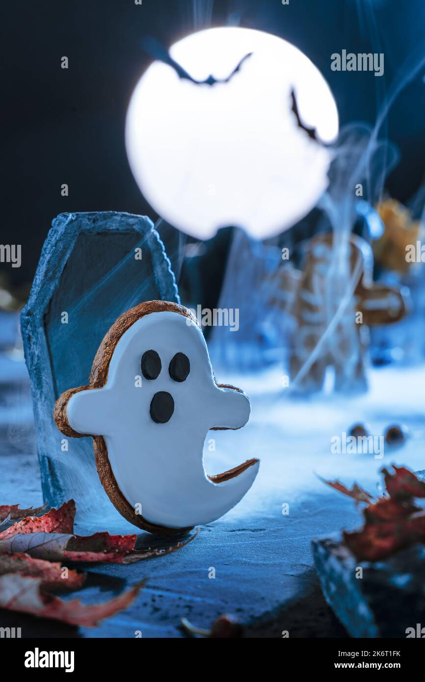 Gruseliger Halloween Hintergrund. Friedhof und Grabsteine in einer gruseligen Nacht und blauem Mondlicht. Fliegende niedliche gruselige Geist Monster, Zombie steigt aus dem GRA Stockfoto