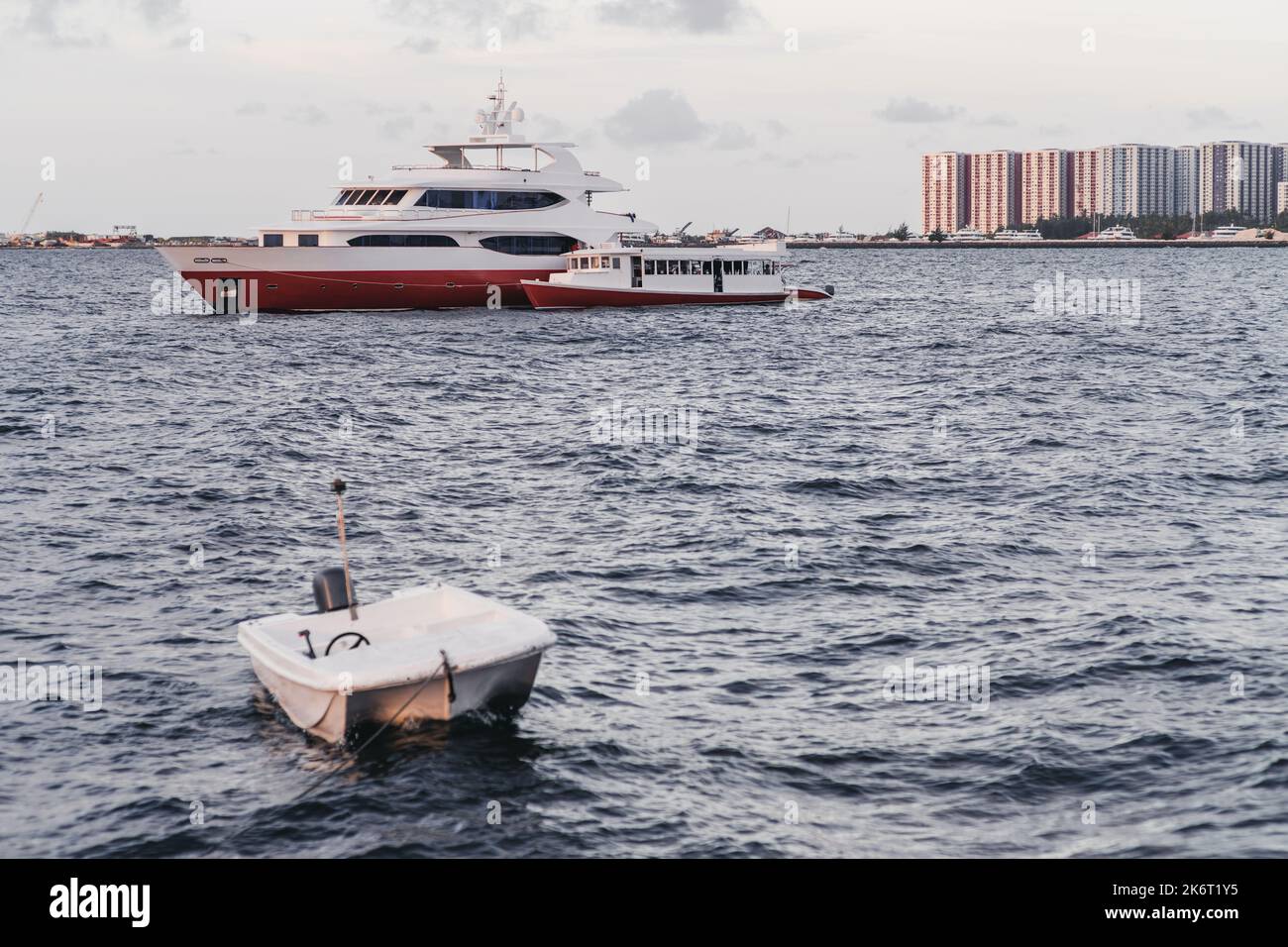 Eine Meereslandschaft mit mehreren Schiffen: Eine luxuriöse Safari-Yacht mit rotem Rumpf und ein kleineres Doney-Boot, das im Hintergrund daran festgemacht ist; ein kleiner Motor Stockfoto