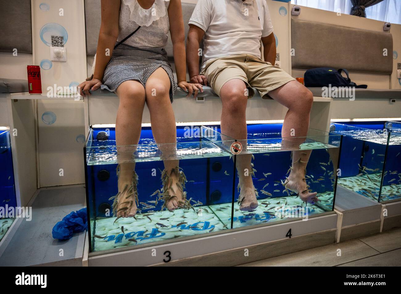 Ein paar asiatische Touristen genießen eine Fisch-Pediküre, auch bekannt als Fisch-Spa-Behandlung, wo die Kunden ihre Füße in einer Wanne mit Wasser gefüllt mit Witz Stockfoto