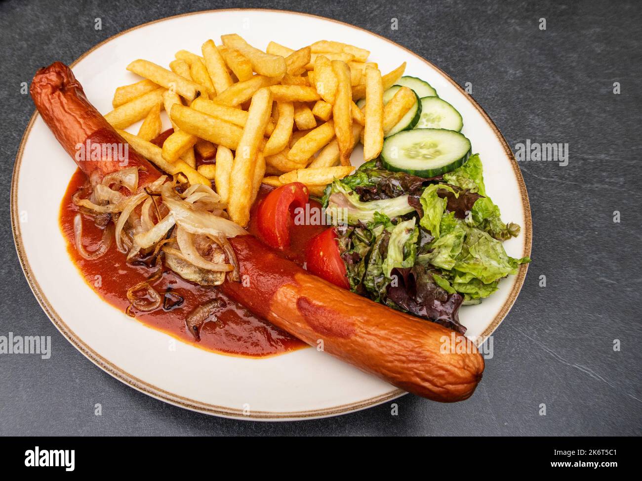 Frittierte Currywurst mit Pommes Frites, Salat und gebratenen Zwiebeln Stockfoto