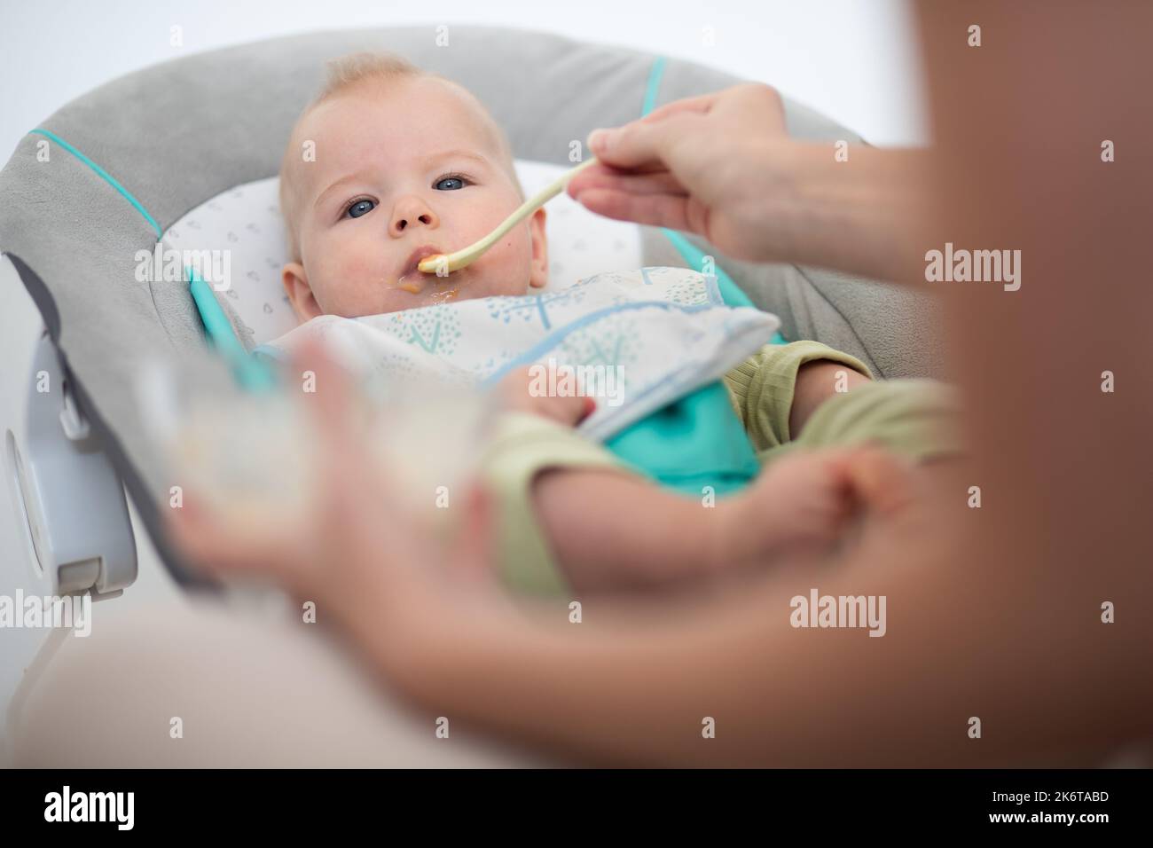 Mutter Löffel Fütterung ihres kleinen Jungen Kleinkind in Babystuhl mit Fruchtpüree. Baby feste Nahrung Einführung Konzept. Stockfoto