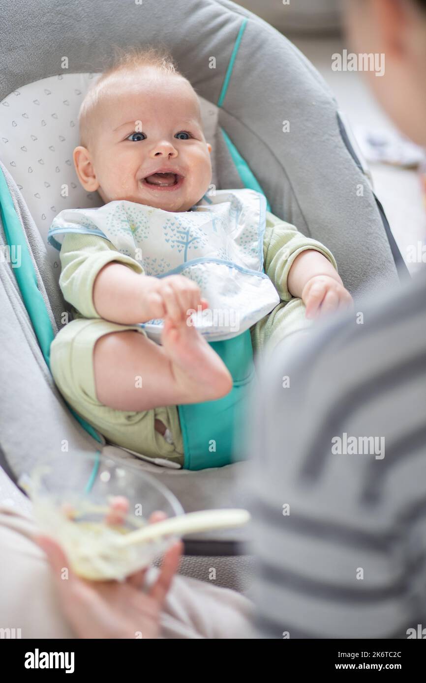 Mutter Löffel Fütterung ihres kleinen Jungen Kleinkind in Babystuhl mit Fruchtpüree. Baby feste Nahrung Einführung Konzept. Stockfoto