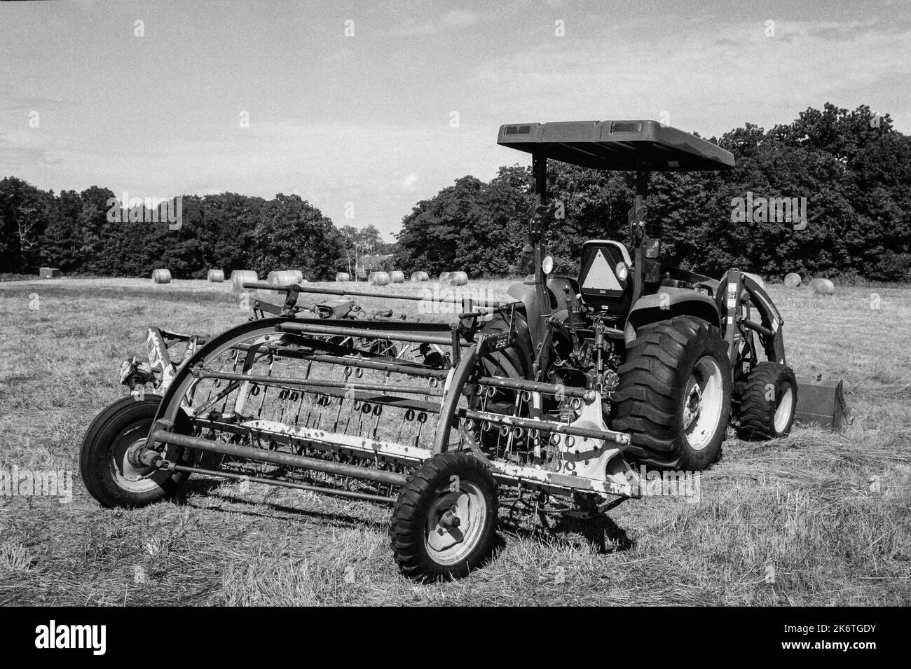Ein Heurake und ein Tracktor auf einem Feld an einem sonnigen Tag im Cogswell Grant im historischen Essex, Massachusetts. Das Bild wurde mit analogem Schwarzweiß aufgenommen Stockfoto