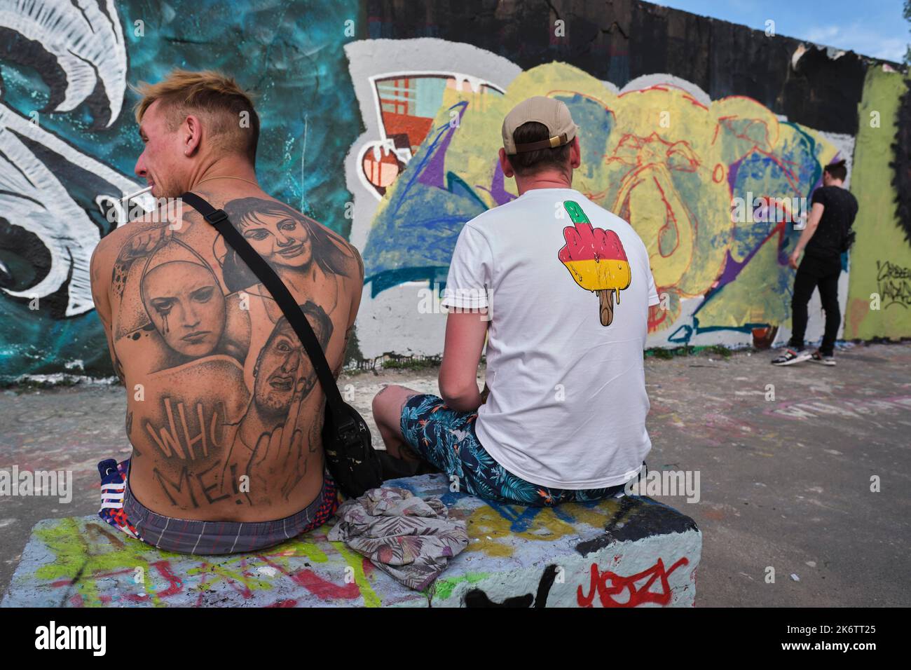 Deutschland, Berlin, 09. 05. 2021, Sonntagnachmittag im Mauerpark, Graffiti-Wand, zwei Männer, tätowiert zurück, stinkender Finger, T-Shirt Stockfoto