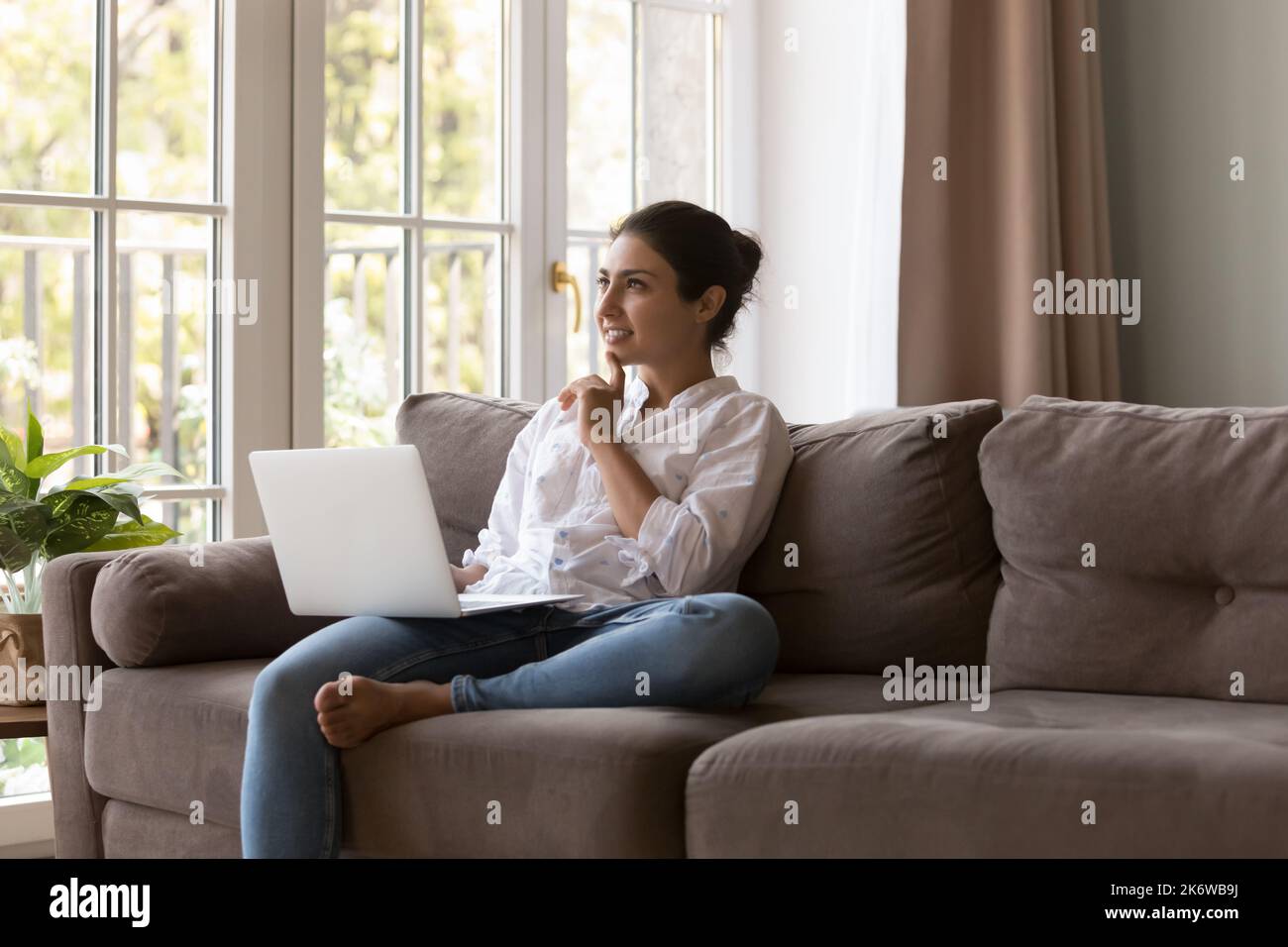 Nachdenkliche junge indische Frau sitzt auf der Couch mit Laptop Stockfoto
