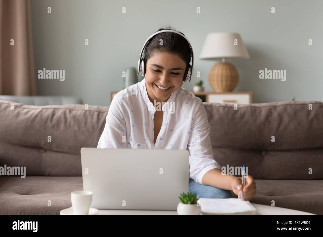 Fröhliche indische Frau in Kopfhörern mit Laptop zu Hause lernen Stockfoto