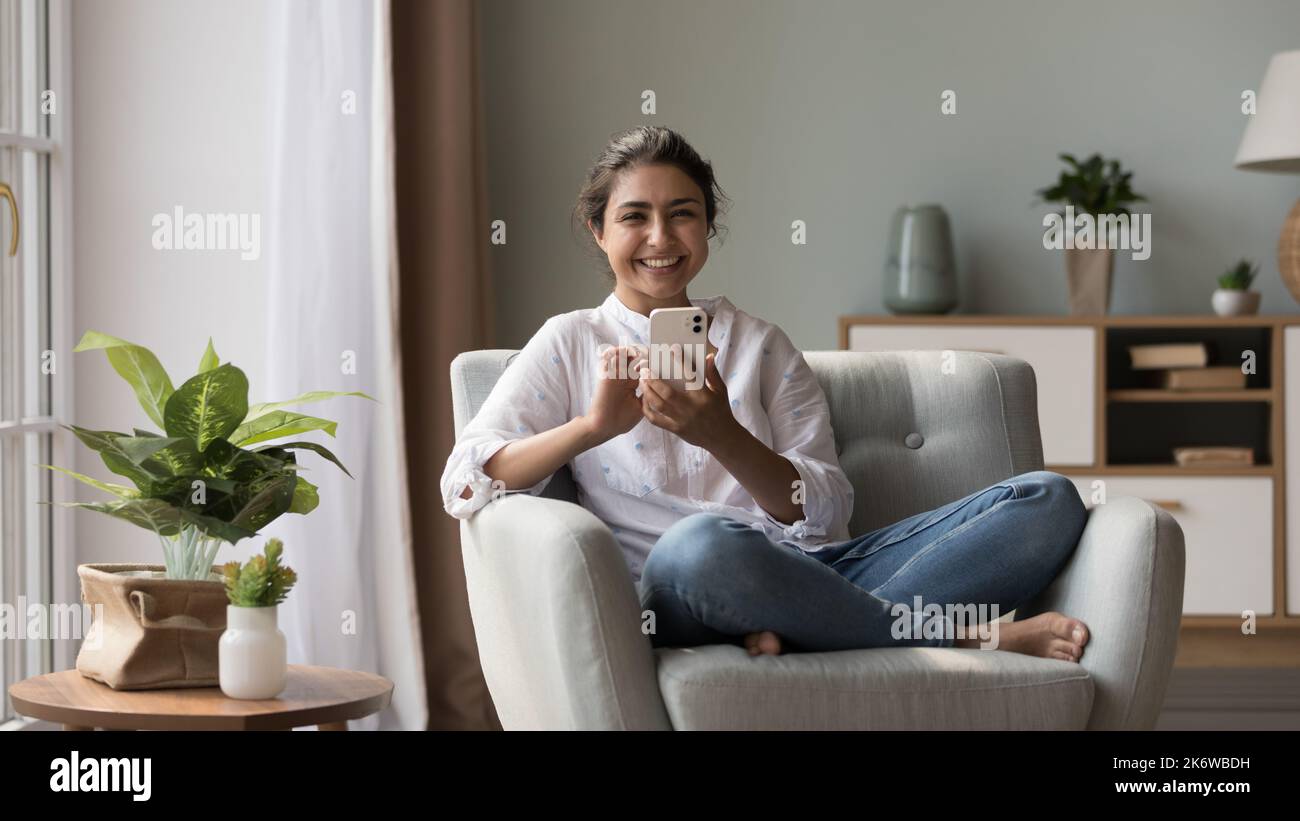 Lächelnde indische Frau hält modernes Handy schaut auf die Kamera Stockfoto