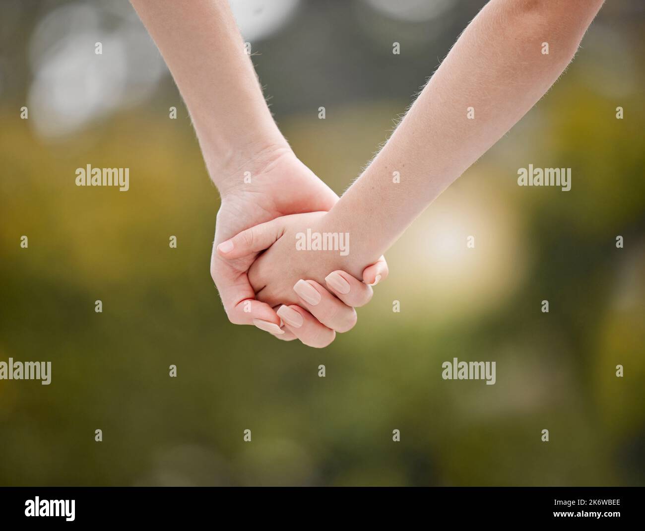 Nahaufnahme einer Mutter, die ihre Kinder in der Hand hält, während sie an einem sonnigen Tag draußen gegen das Grün geht. Ein Elternteil wird die Familie führen, schützen und schützen Stockfoto