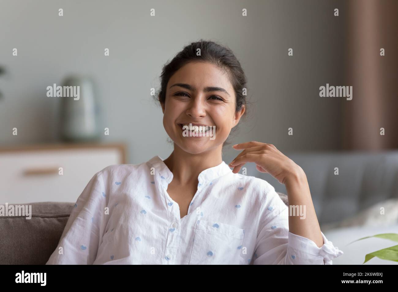 Fröhliche indische Frau sitzt auf der Couch Lächeln starrte auf die Kamera Stockfoto
