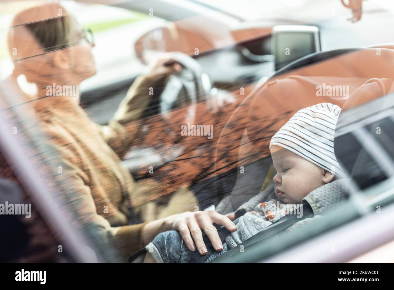 Mutter konzentriert sich darauf, mit dem Familienauto Besorgungen zu machen, während ihr Baby auf dem Kindersitz neben ihrem Standort schläft. Stockfoto