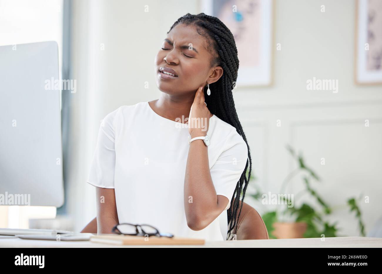 Zu viele Stunden, die über einen Schreibtisch gejagt wurden. Eine junge Geschäftsfrau, die bei der Arbeit einen Nackenkrampf erlebt. Stockfoto