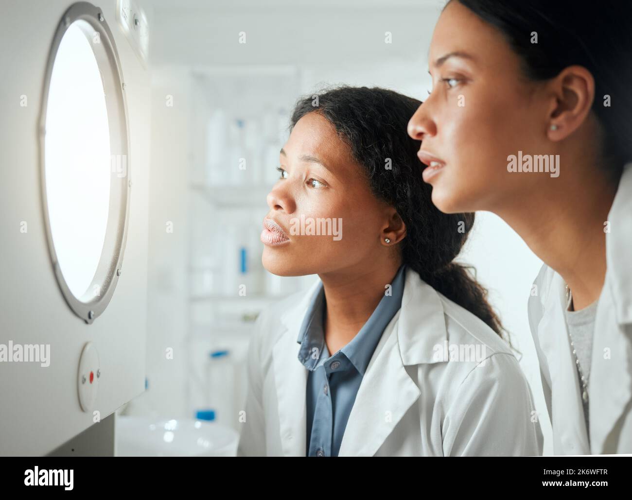 Wie viel länger wird es dauern. Zwei Wissenschaftlerinnen blicken durch eine Tür und warten auf Ergebnisse. Stockfoto