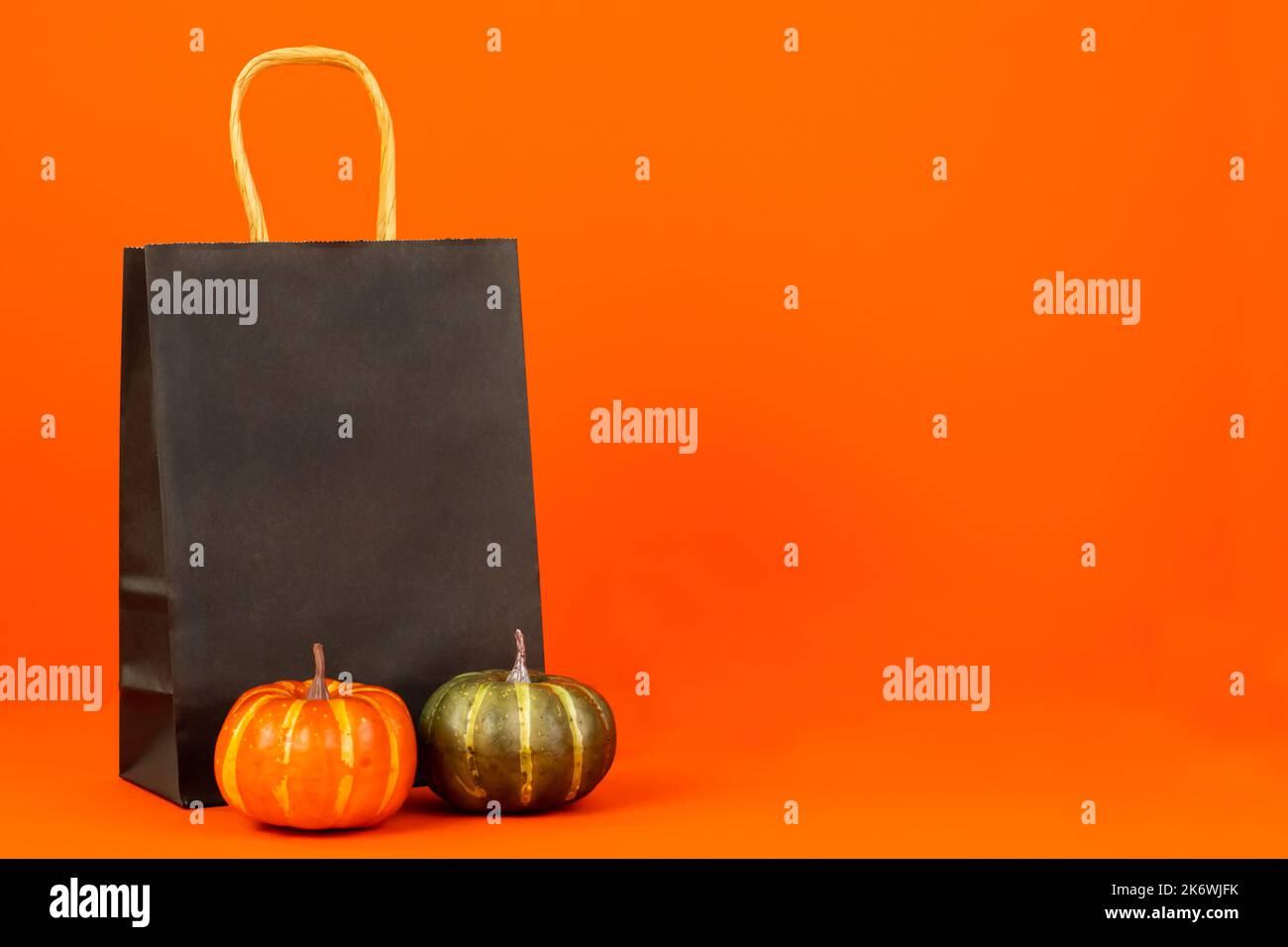 Halloween. Schwarzes Papierpaket, Kürbisse stehen neben einem orangefarbenen Hintergrund. Stockfoto