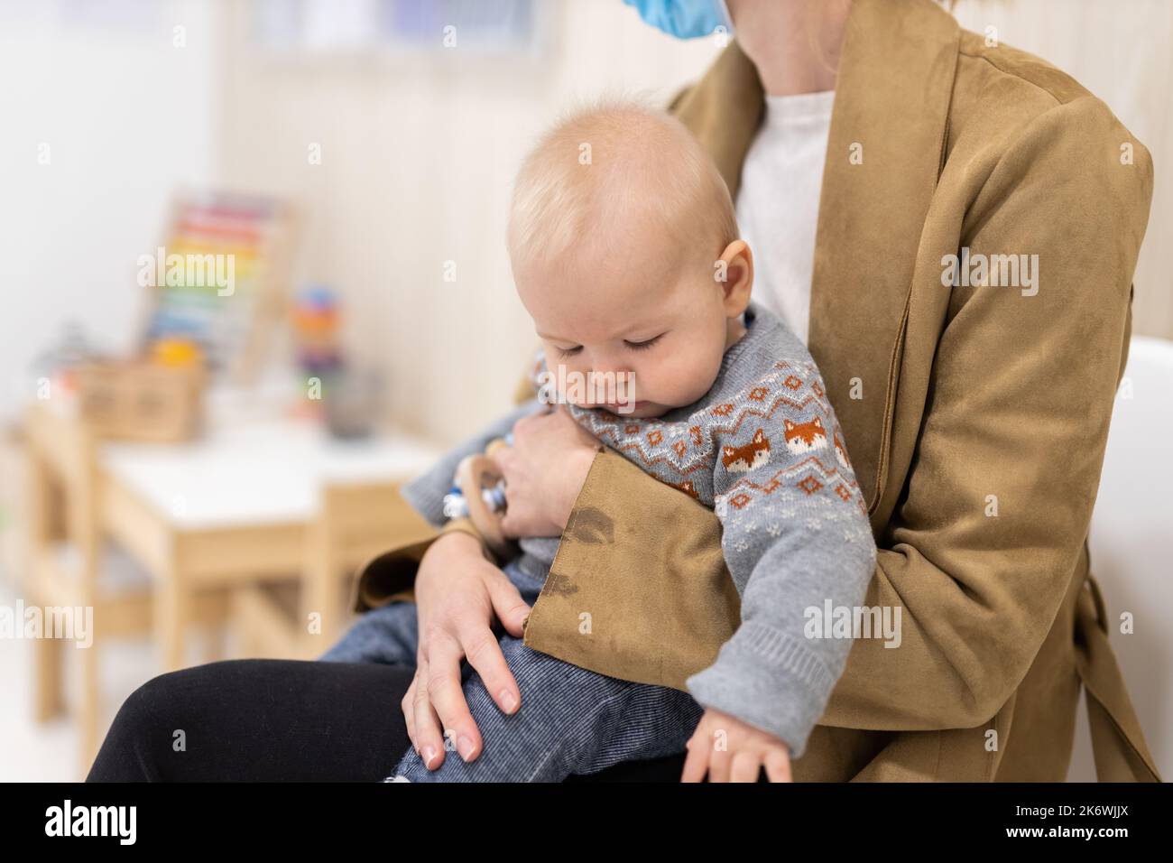 Mutter hält einen kleinen Jungen in ihrem Schoß, sitzt und wartet vor der Arztpraxis auf einen pädiatrischen Brunnencheck. Gesundheitskonzept des Kindes Stockfoto